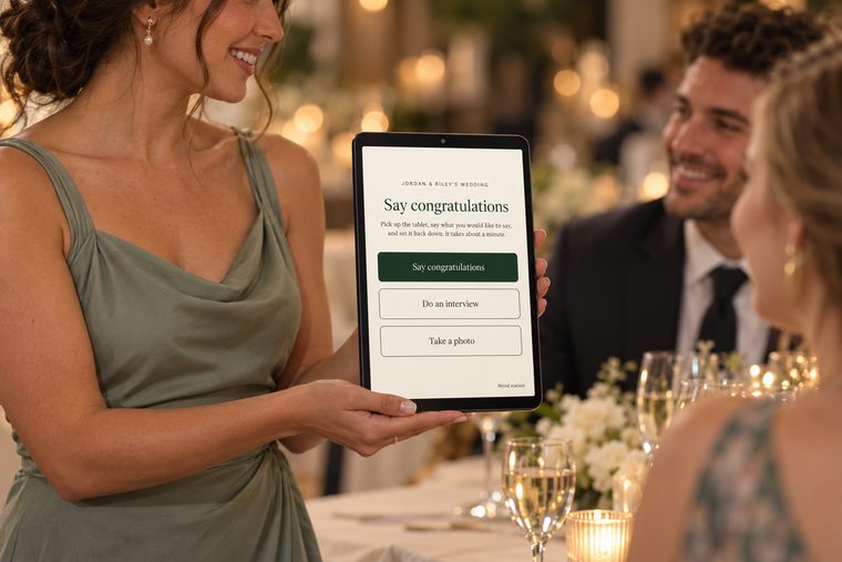A friend holds a tablet station out to guests at a reception table, smiling, inviting them to say congratulations